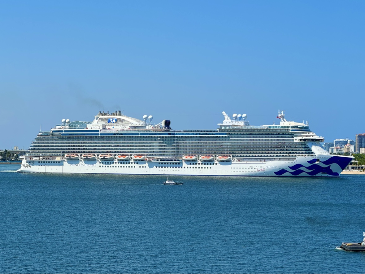 Princess Cruises' Enchanted Princess in full broadside, her blue wave livery painted on the bow, with a small pilot boat alongside