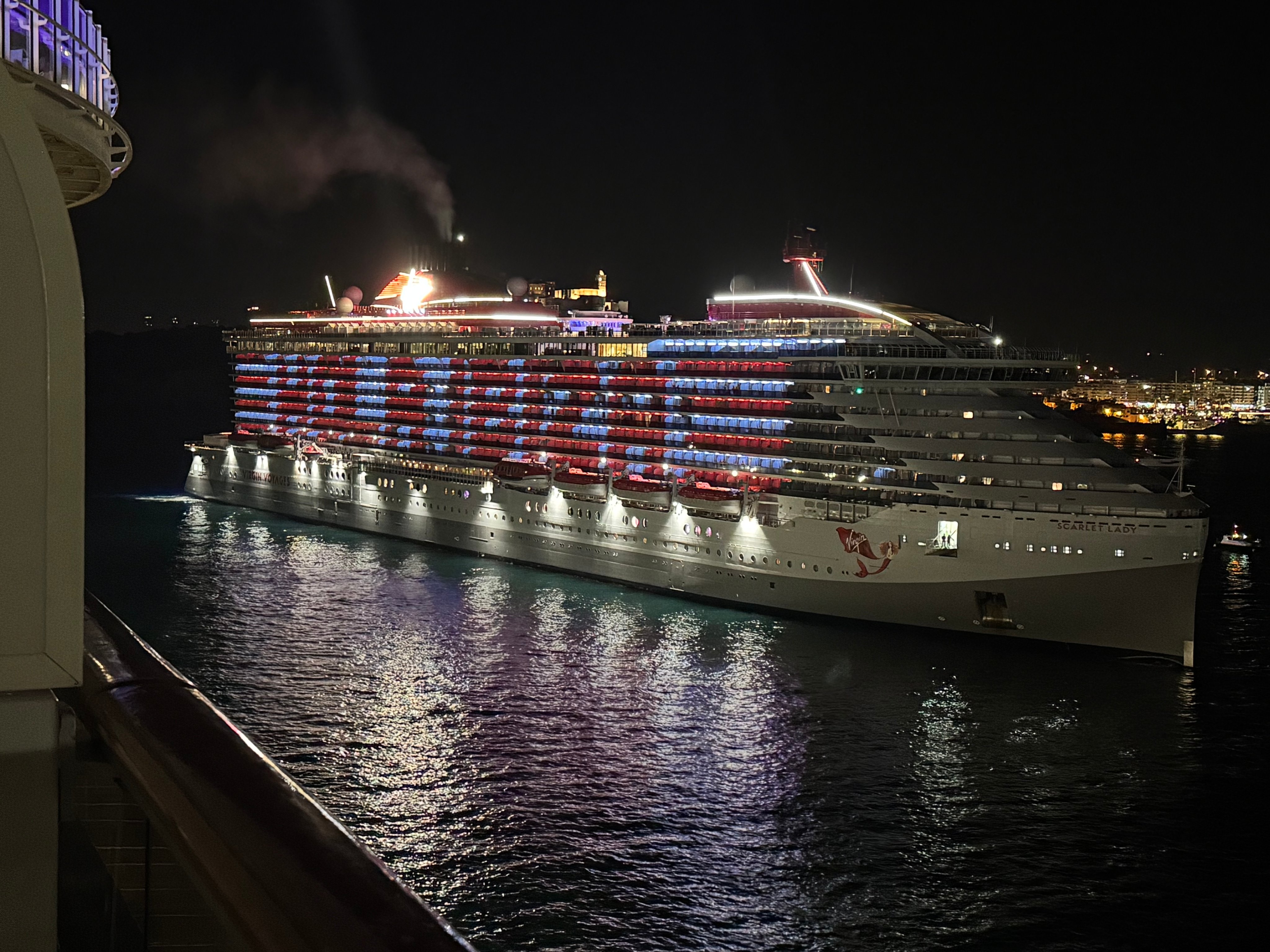 Virgin Voyages' Scarlet Lady lit up at night in Ibiza, balcony lights glowing red and blue